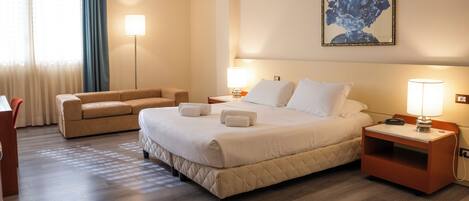 Une chambre d’hôtel avec un grand lit, deux tables de chevet, un canapé, une lampe sur pied et un tableau au mur.