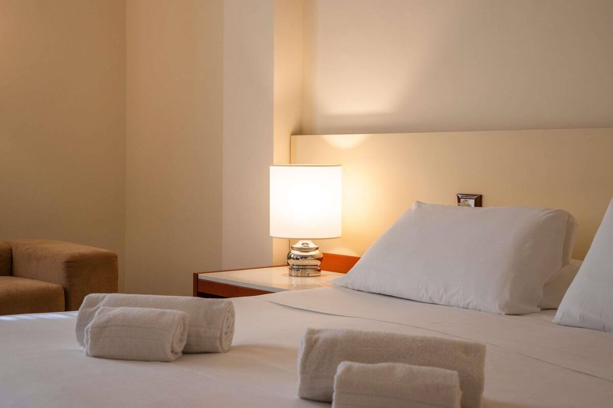 A hotel room with a bed, a nightstand, a lamp, and a chair.