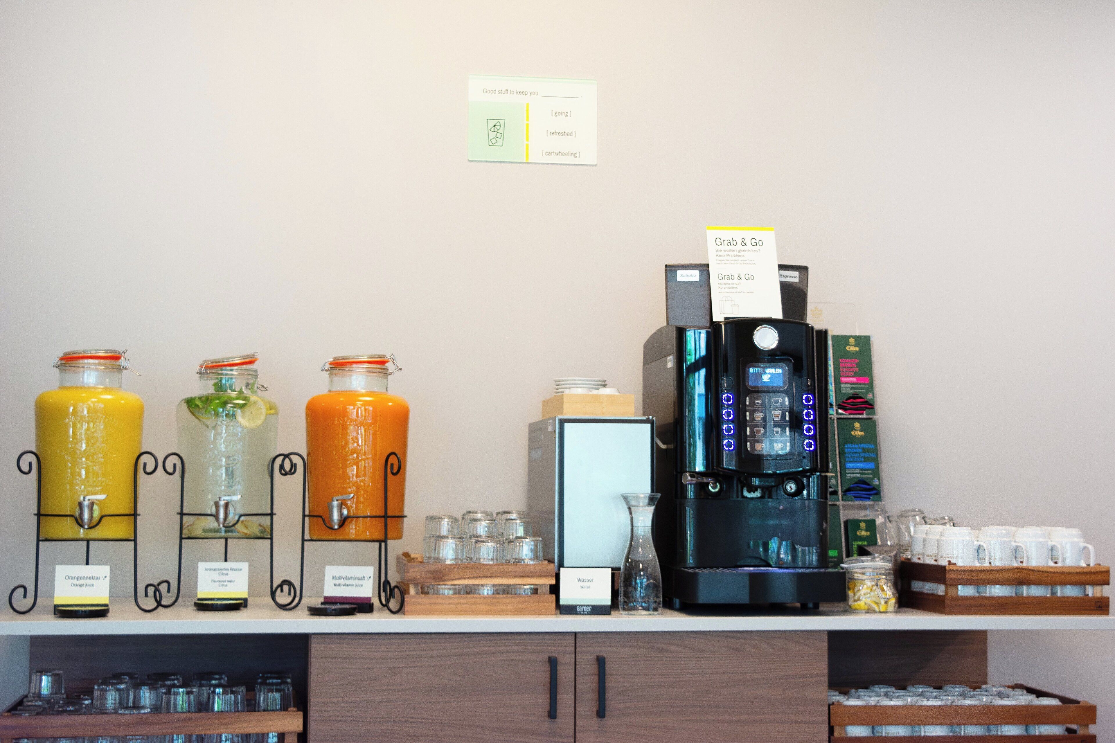 Una estación de bebidas con tres dispensadores, una máquina de café y varios recipientes.