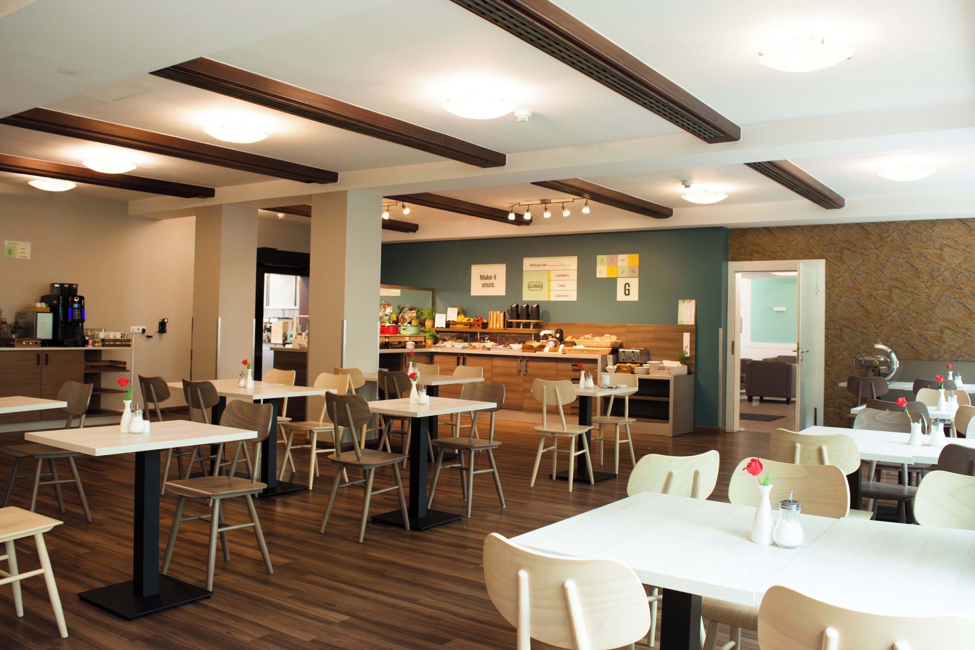A modern restaurant interior with multiple dining tables and chairs, a kitchen area in the background, and a bar.