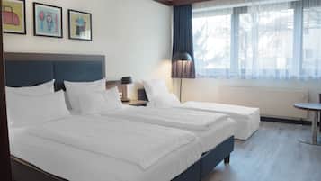 A hotel room with two beds, a nightstand, a lamp, and a window with curtains.