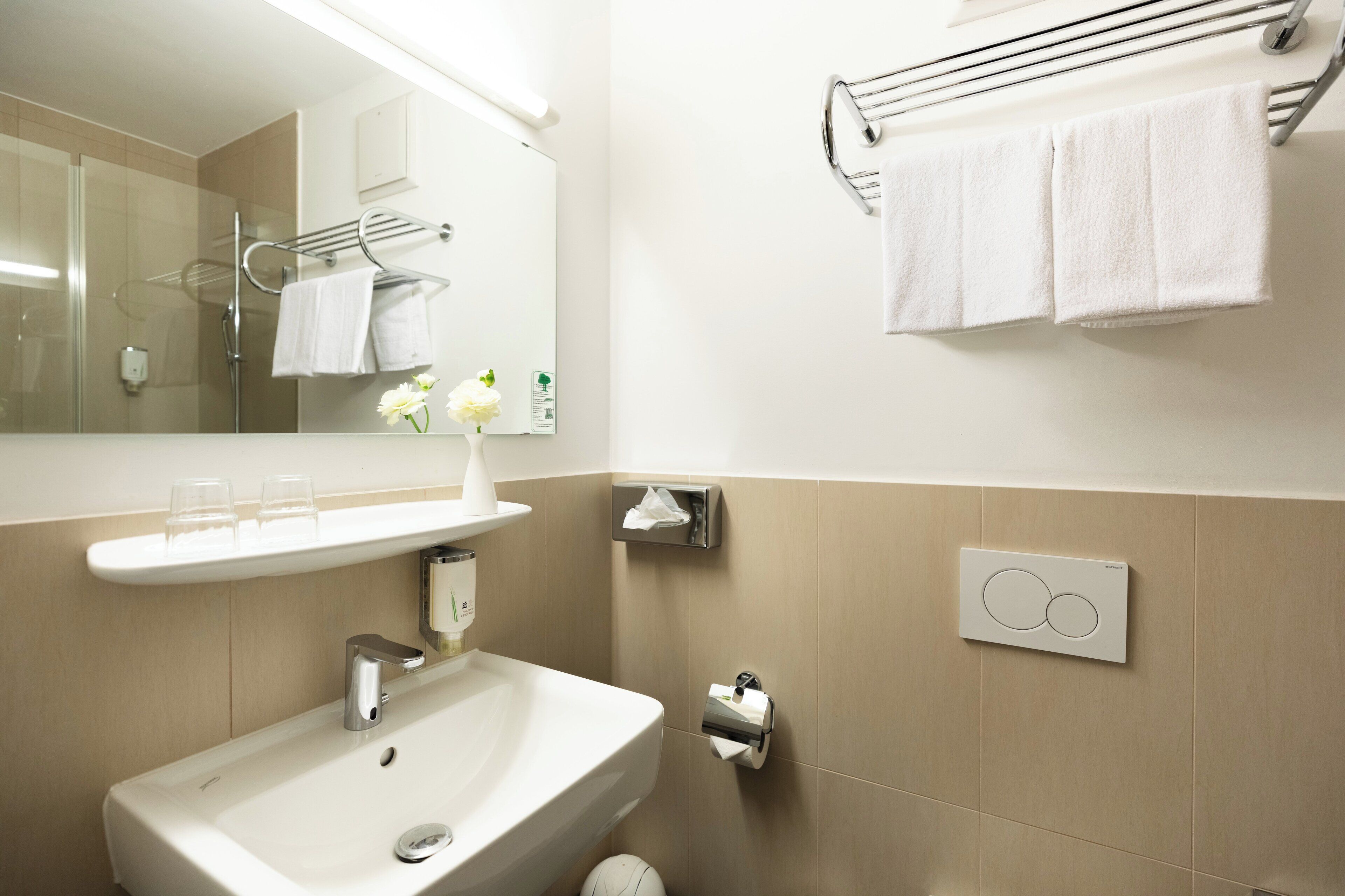 A modern bathroom with a sink, mirror, towel rack, and a wall-mounted towel dispenser.