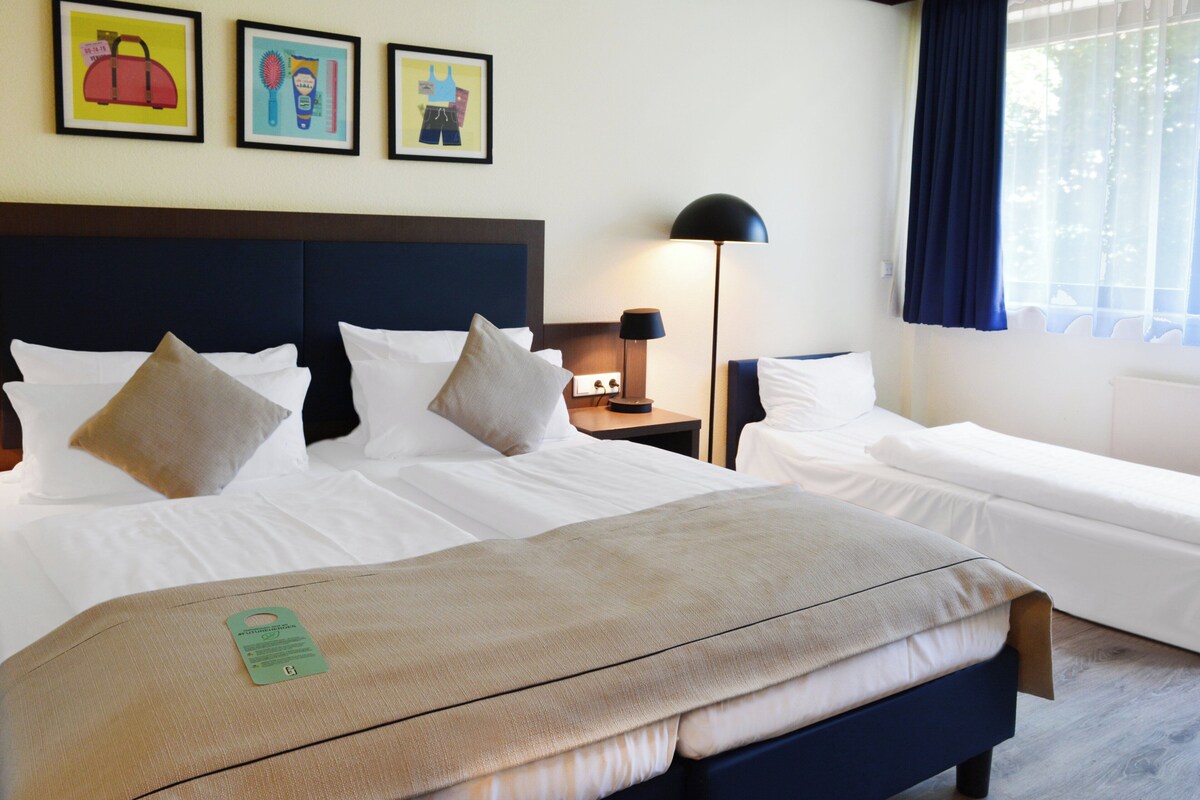 A hotel room with a large bed, a smaller bed, a nightstand with a lamp, and artwork on the wall.