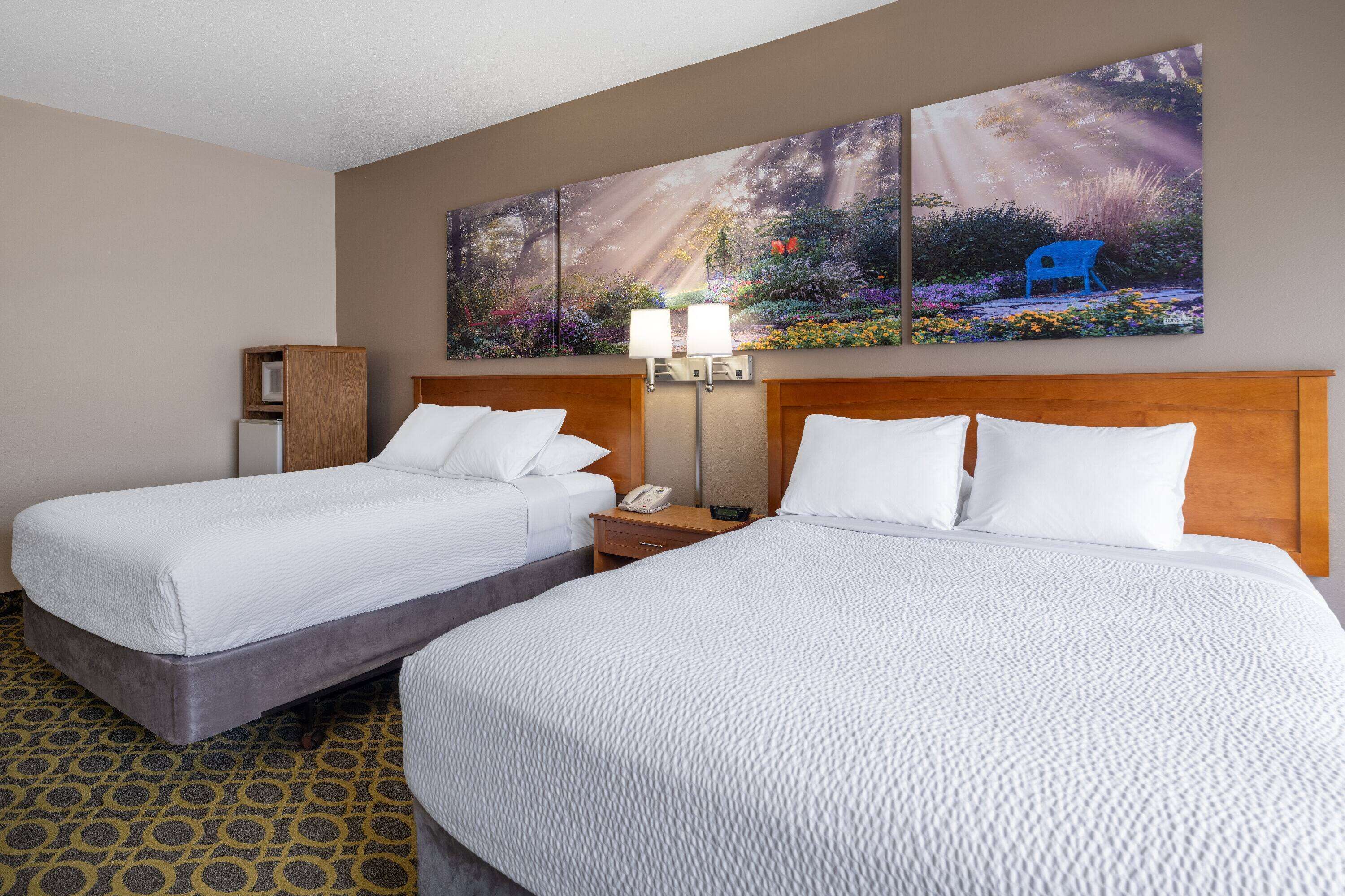 A hotel room with two beds, a nightstand with a lamp, and a painting on the wall.