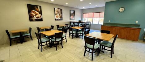 A restaurant with multiple tables and chairs, a kitchen area, and a clock on the wall.