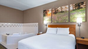 A hotel room with a large bed, a separate bathtub, and two wall-mounted lamps.
