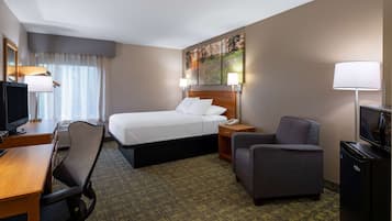 Ein Hotelzimmer mit einem Bett, einem Schreibtisch mit Stuhl, einem Fernseher, einer Lampe und einem Kühlschrank.