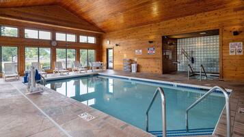An indoor swimming pool with wooden walls, a clock, and a lifeguard chair.