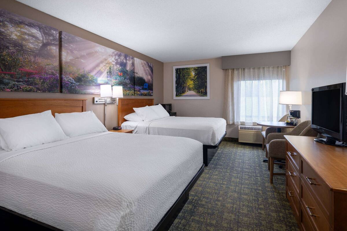 A hotel room with two beds, a desk, a TV, and artwork on the walls.
