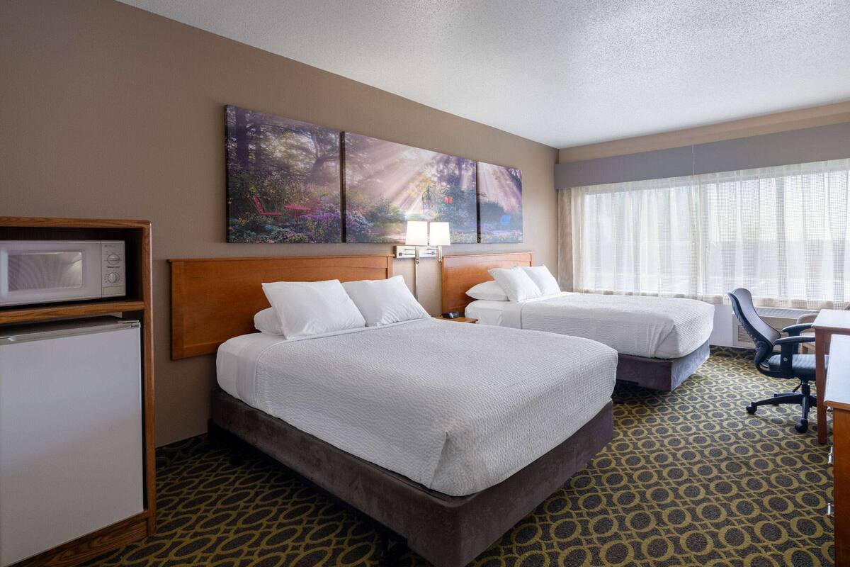 A hotel room with two beds, a desk, a chair, a microwave, and a refrigerator.