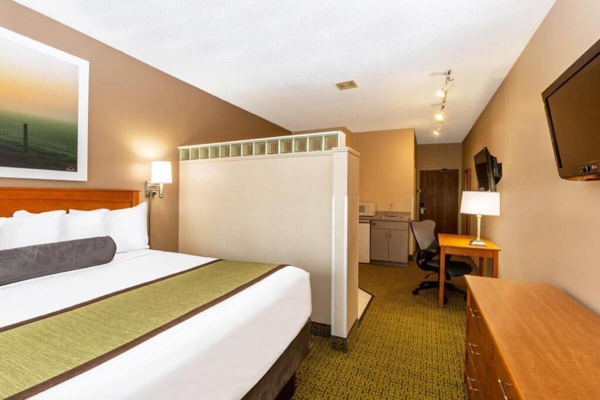A hotel room with a bed, desk, chair, and kitchenette.