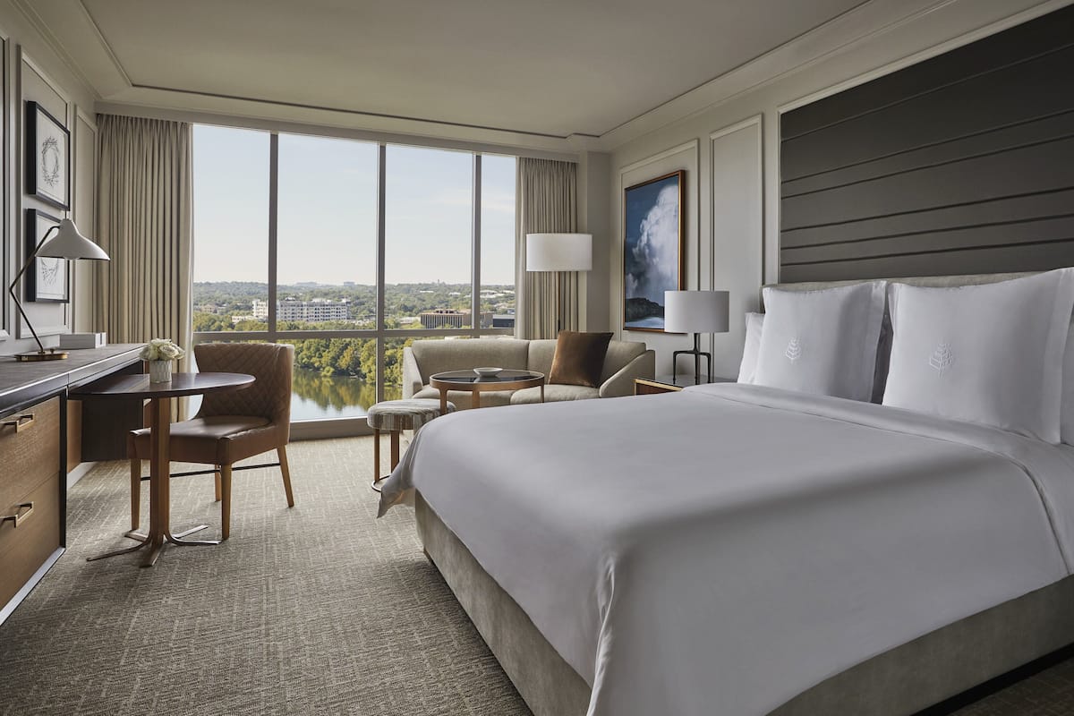 Ein Hotelzimmer mit einem großen Bett, einem Schreibtisch, einem Sessel und einem kleinen Tisch, mit Blick auf die Stadt.