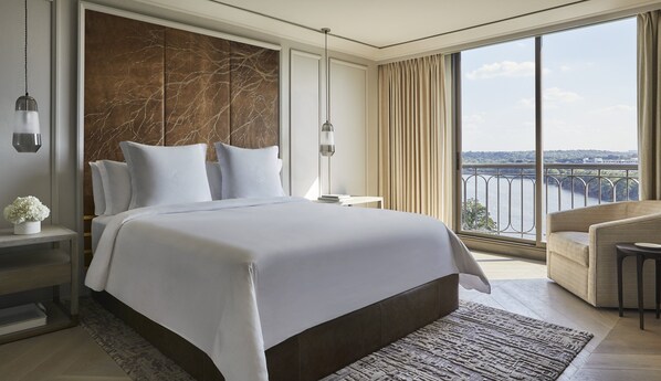 A modern hotel room with a large bed, a view of a river, and a balcony with a railing.