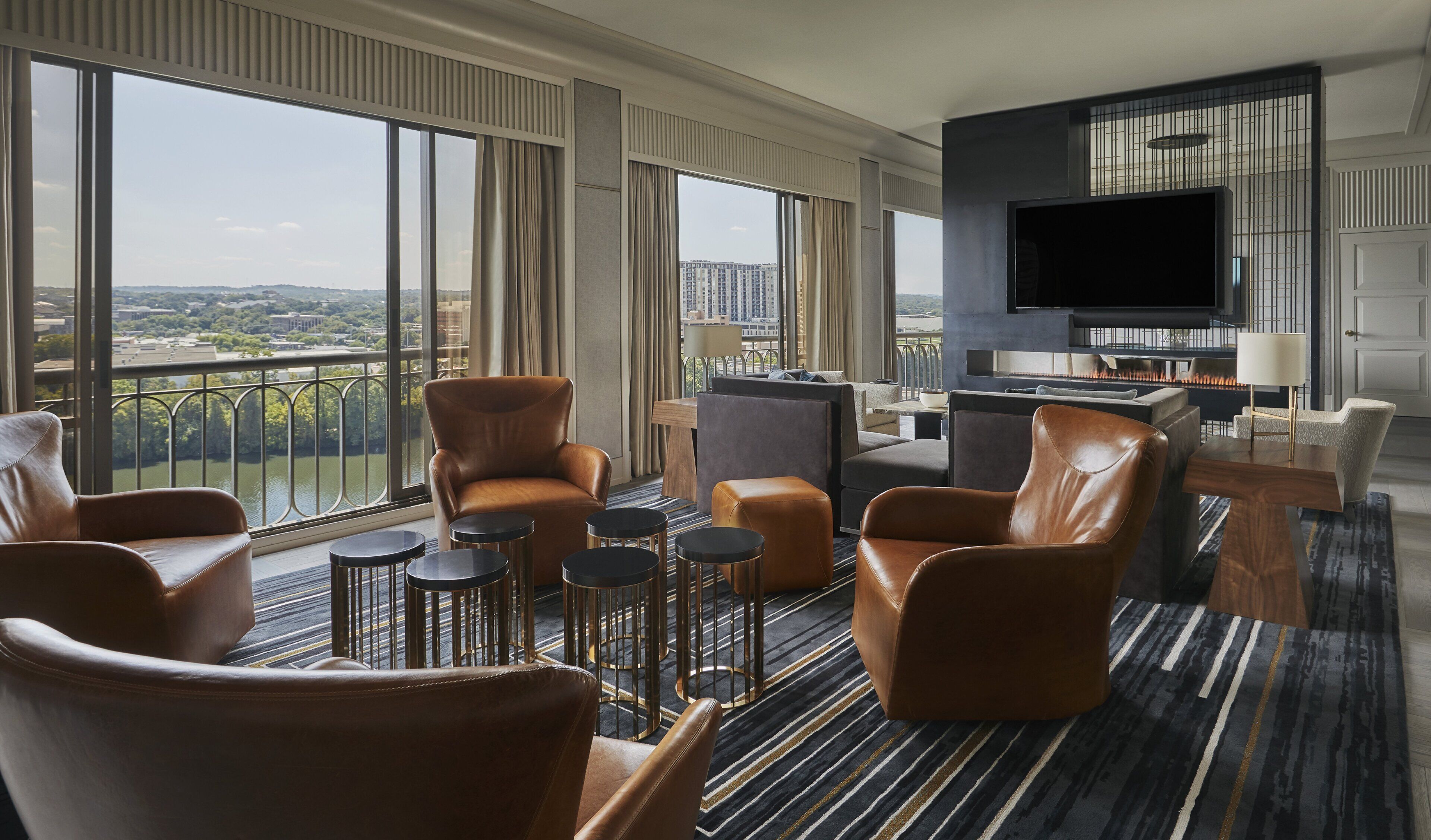 A modern hotel room with leather furniture, a flat-screen TV, and a balcony with a city view.