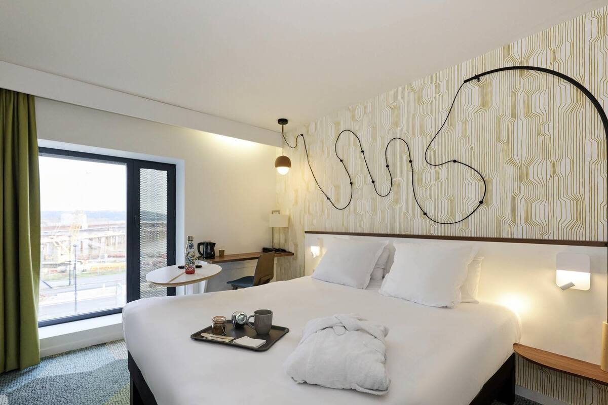 A hotel room with a large bed, a desk, a chair, and a view of the city.
