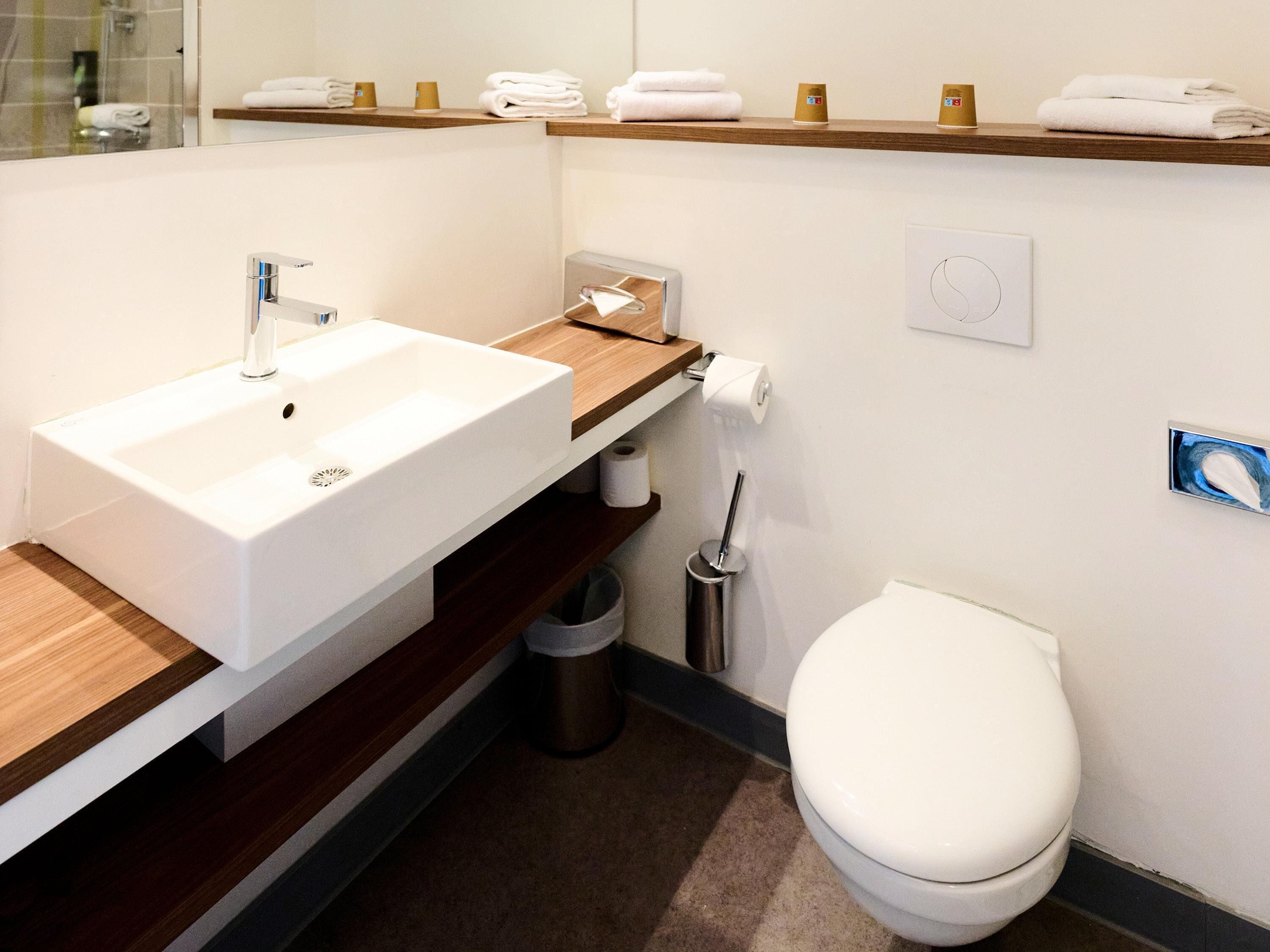 A modern bathroom with a white sink, wooden countertop, and a white toilet.