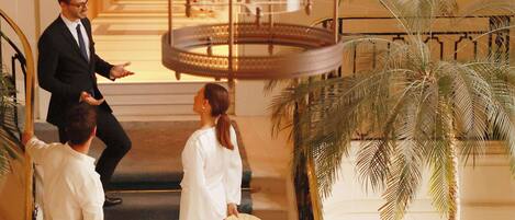 A grand staircase with a palm tree and a woman holding a hat.