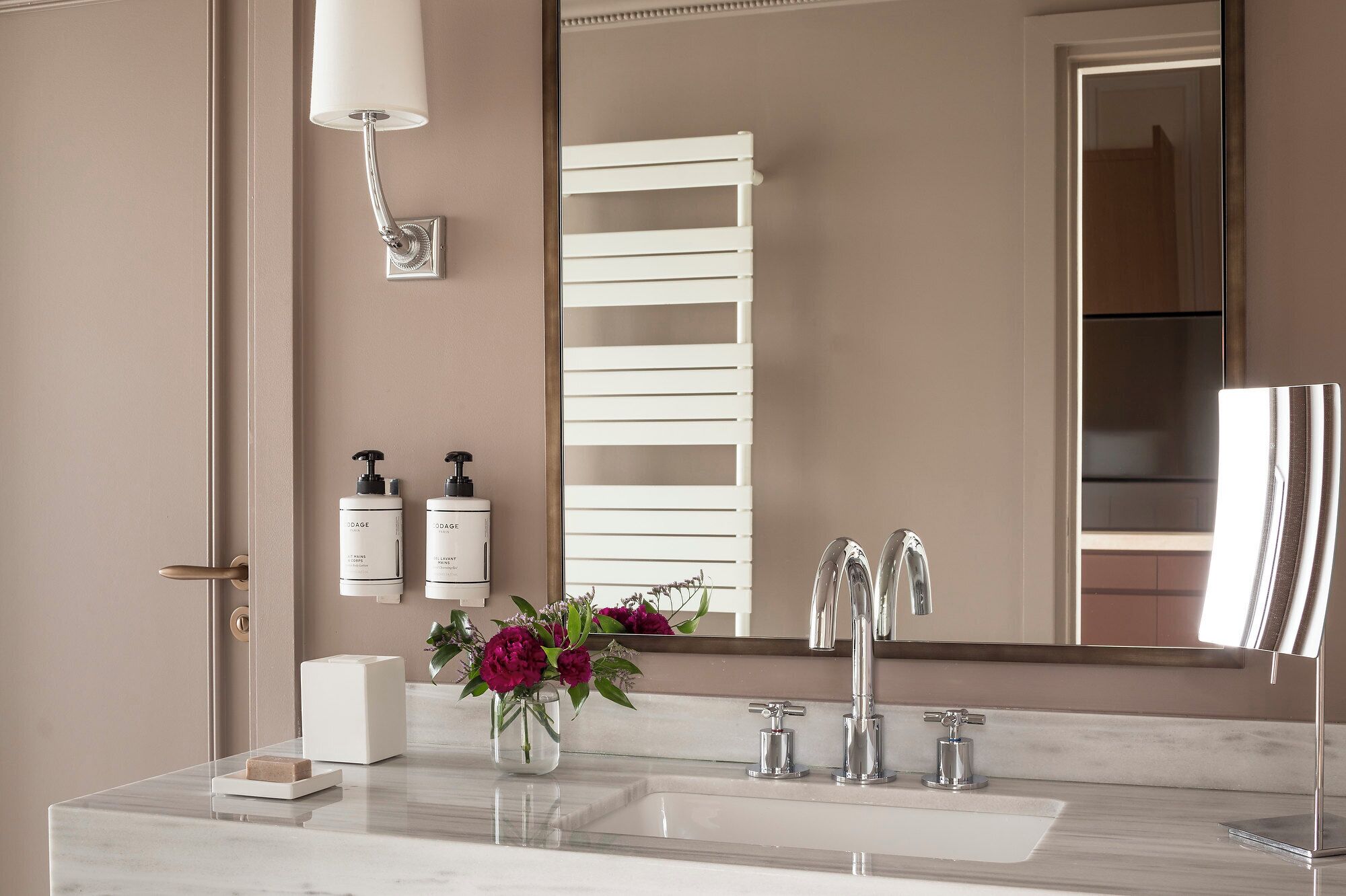 A bathroom with a marble sink, two faucets, a mirror, a towel rack, and two bottles of hand soap.