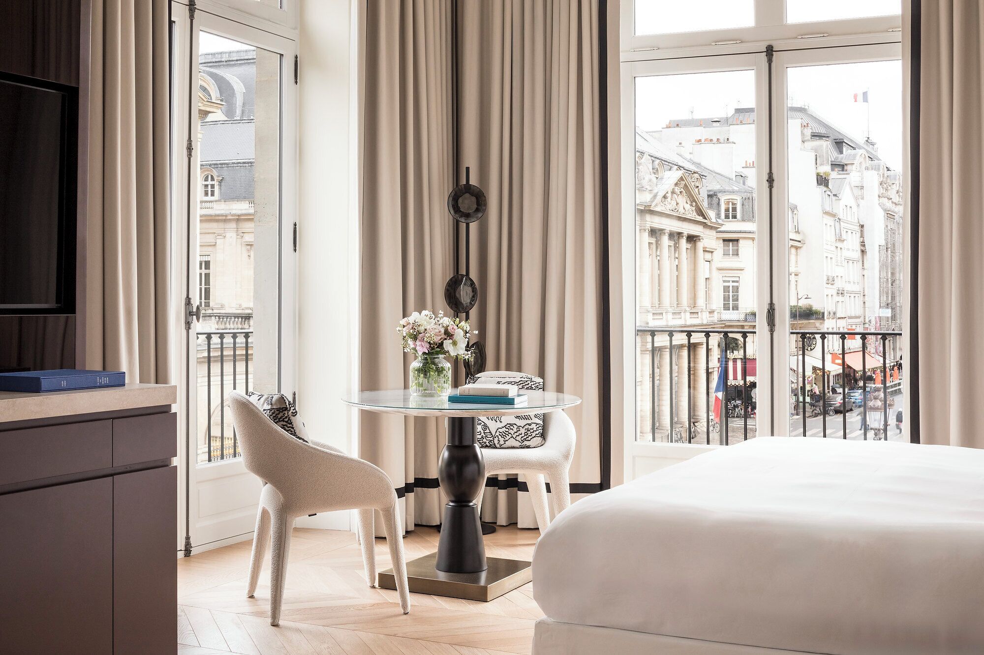 Une chambre d’hôtel avec un lit, une table à manger avec des chaises, un téléviseur et une vue sur le paysage urbain.