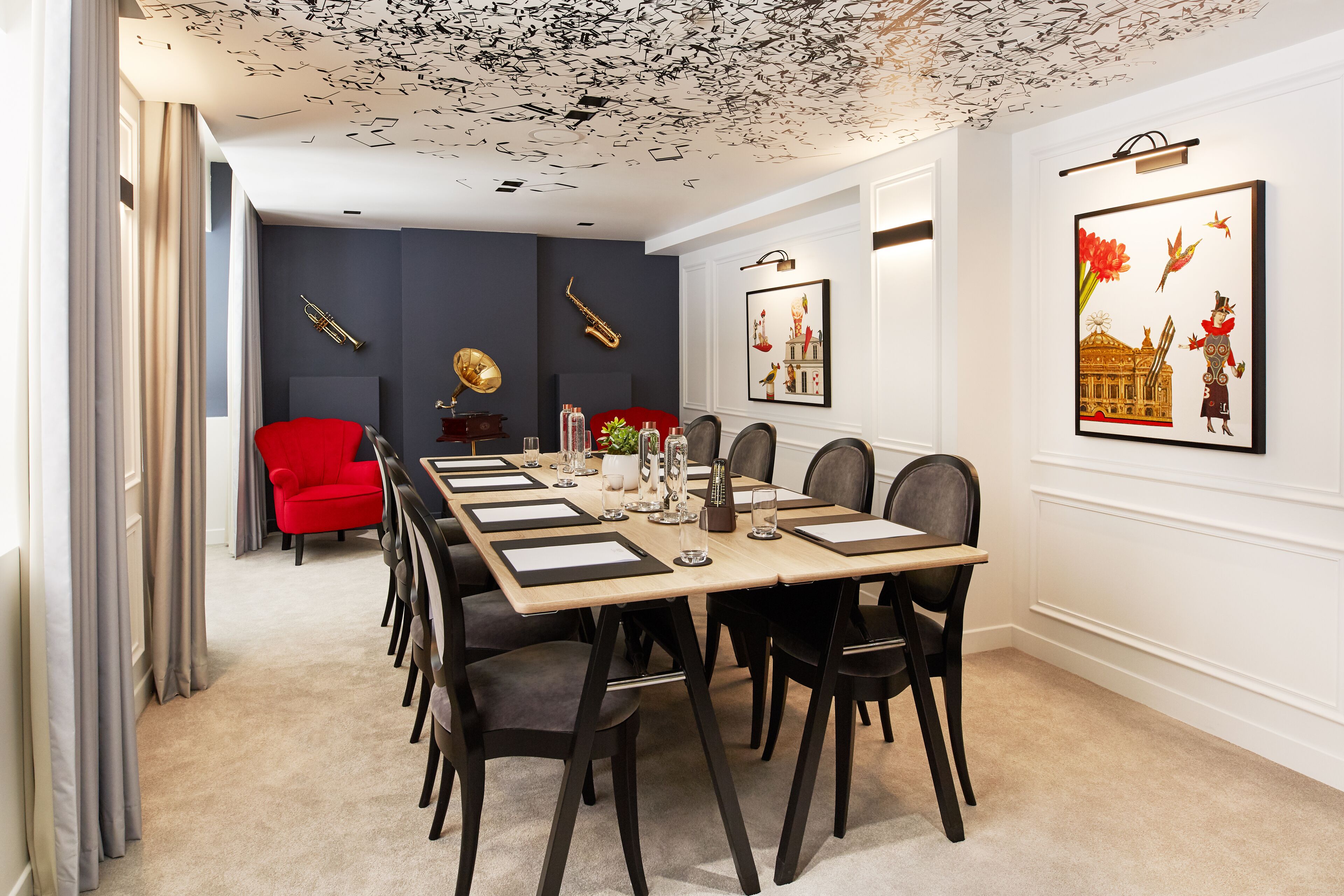 A dining area with a long table set for six, surrounded by chairs, with a red chair in the background.