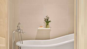 A modern bathroom with a freestanding bathtub, a showerhead, and a shelf with toiletries.