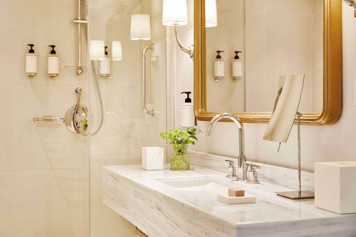 A modern bathroom with a glass shower enclosure, a marble sink, and a large mirror with a gold frame.