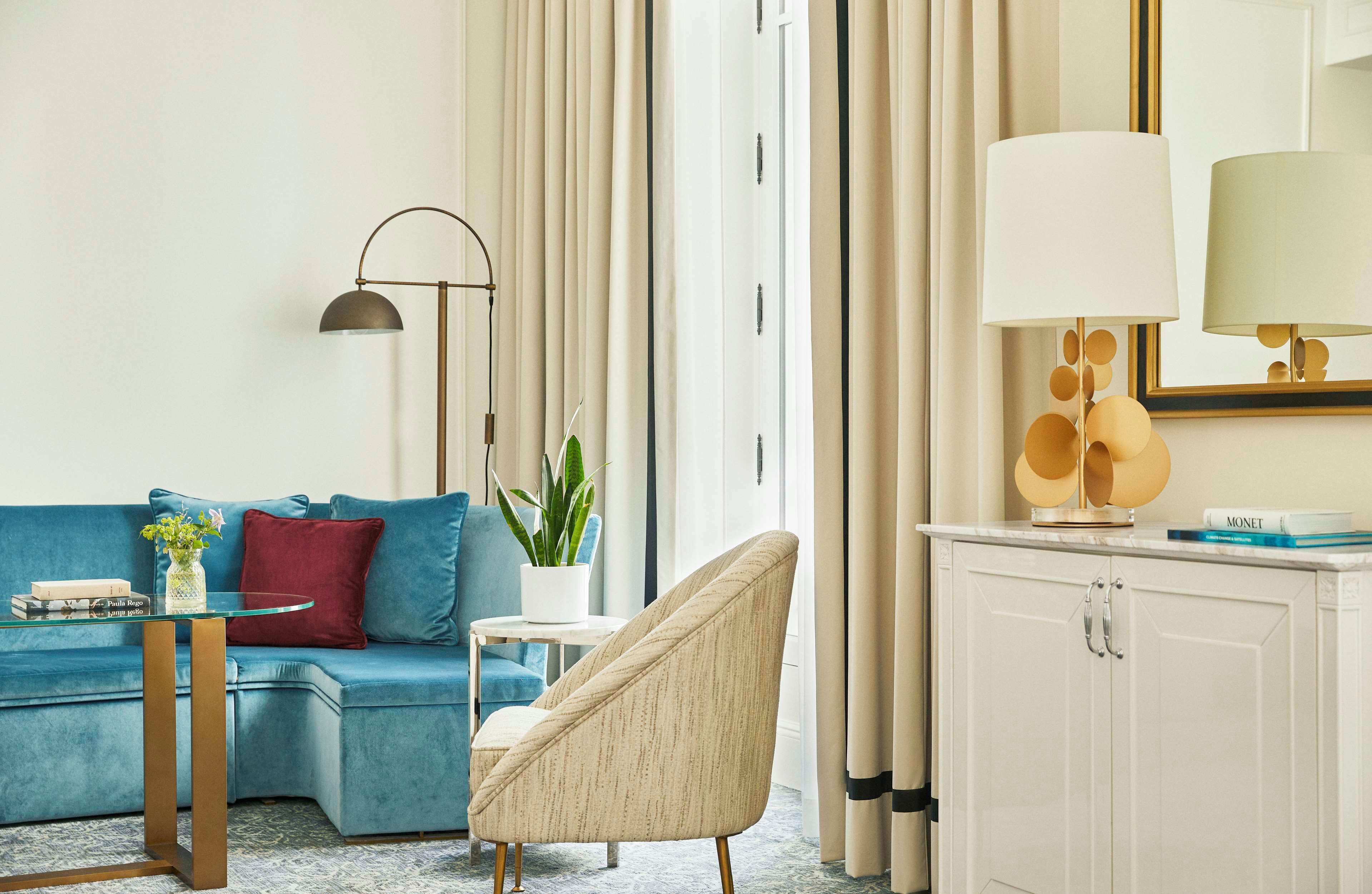 Una sala de estar moderna con un sofá azul, un sillón redondo, una lámpara de pie, una mesita con un florero y un aparador con una lámpara.