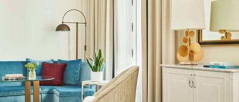 Una sala de estar moderna con un sofá azul, un sillón redondo, una lámpara de pie, una mesita con un florero y un aparador con una lámpara.
