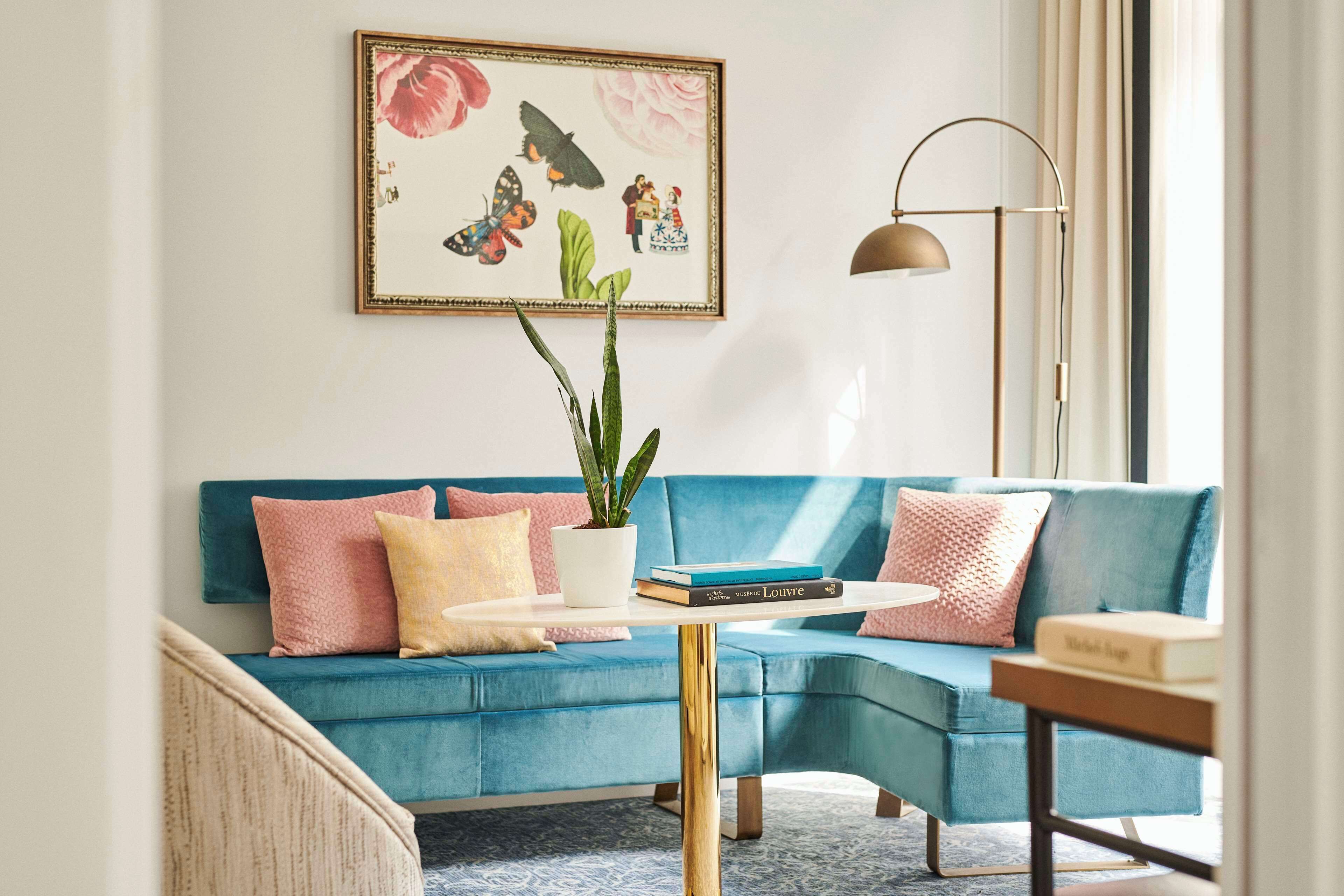 Ein Wohnzimmer mit einem blauen Sofa, einem kleinen runden Tisch, einem Blumentopf und einem gerahmten Bild an der Wand.