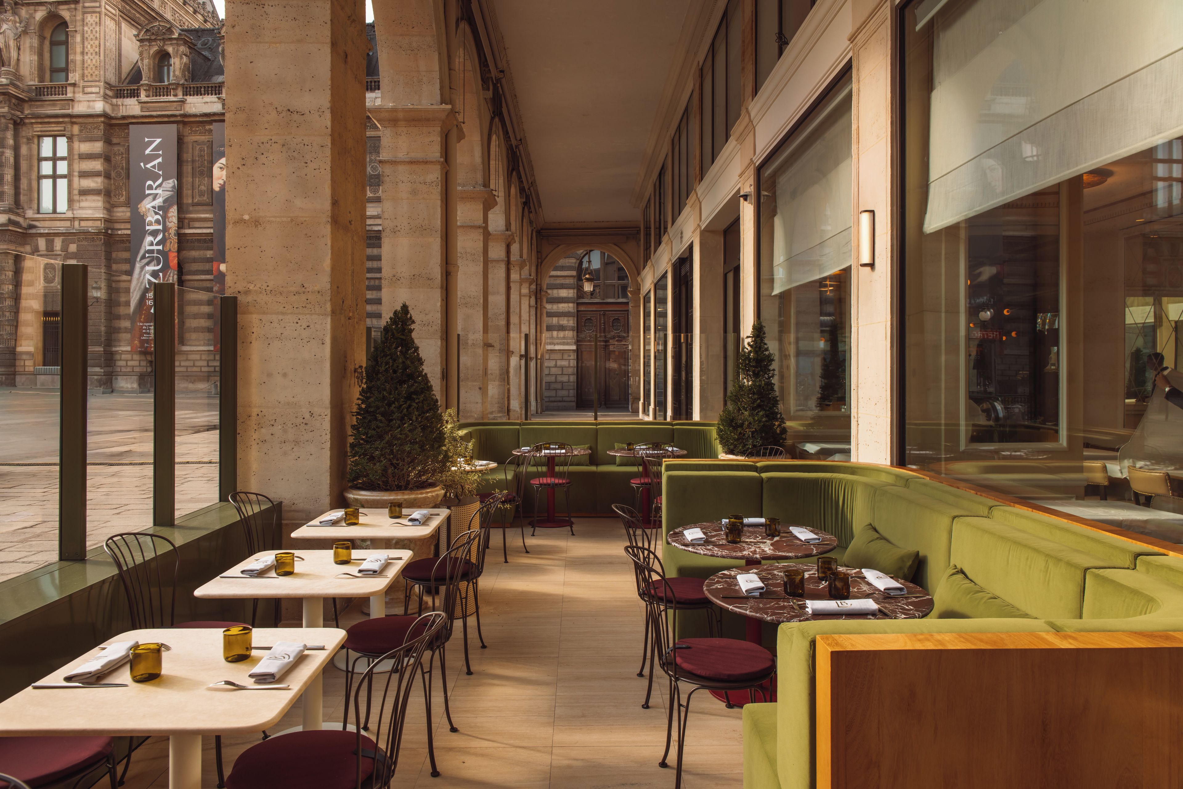 An outdoor cafe with tables and chairs, a green sofa, and a view of a historic building.