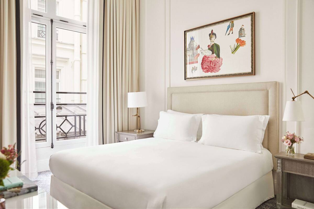 A hotel room with a large bed, a nightstand with a lamp, a framed picture on the wall, and a view of the outside balcony.