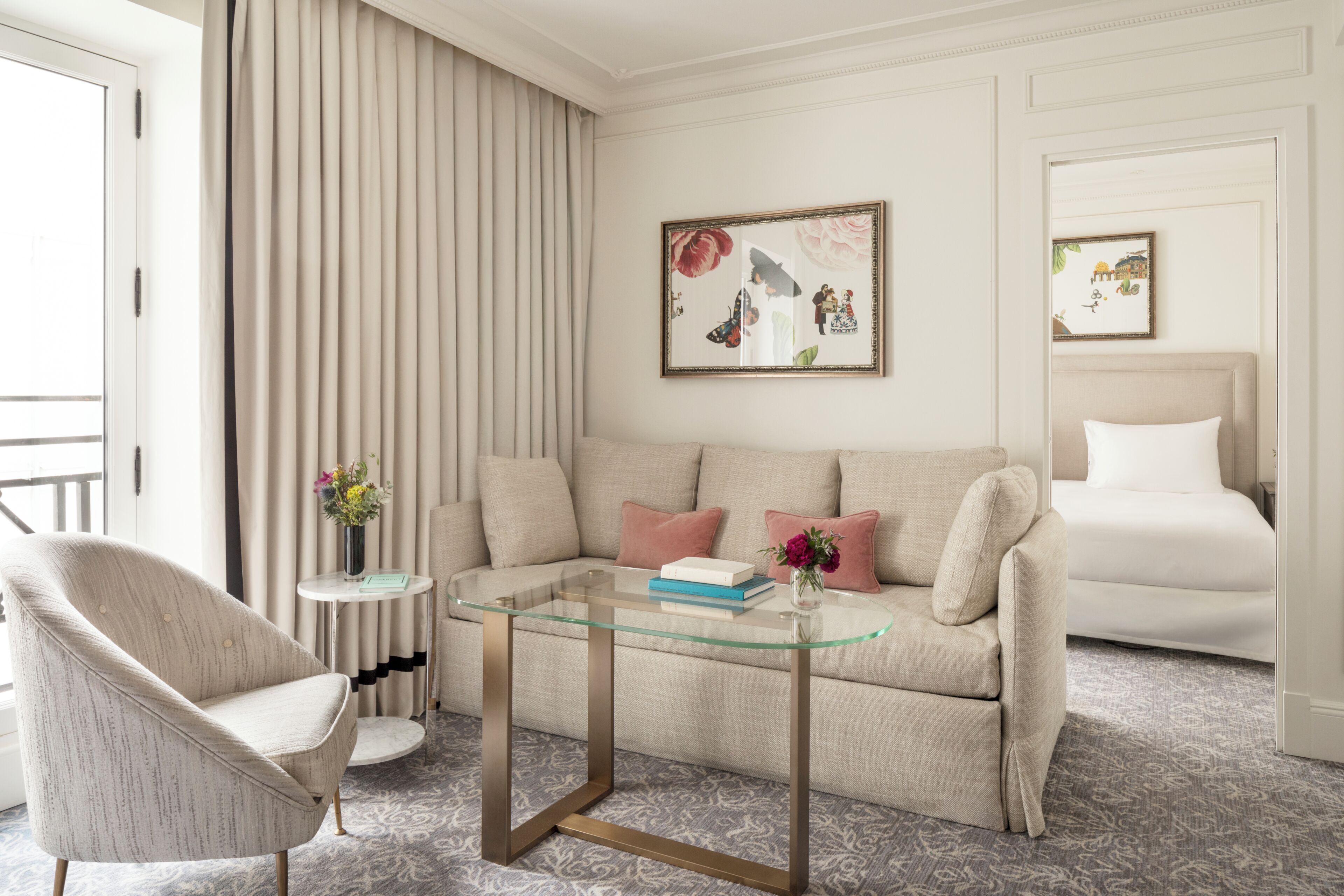 A modern living room with a glass coffee table, a beige sofa, a patterned carpet, and a framed picture on the wall.