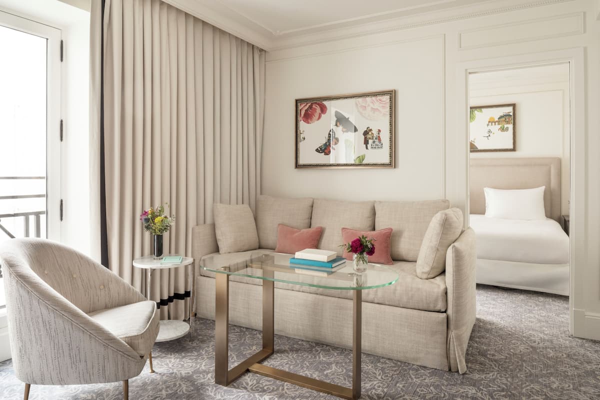 Ein modernes Wohnzimmer mit einem Glastisch, einem beigefarbenen Sofa, einem gemusterten Teppich und einem gerahmten Bild an der Wand.