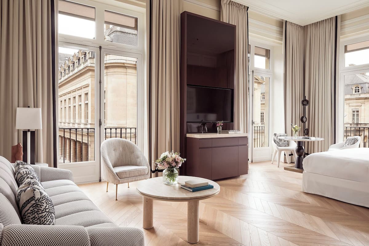 Ein Hotelzimmer mit großem Fenster, Fernseher, Sofa, Esstisch und Bett.