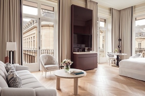 A hotel room with a large window, a television, a sofa, a dining table, and a bed. - Hôtel du Louvre, in The Unbound Collection by Hyatt (Paris)