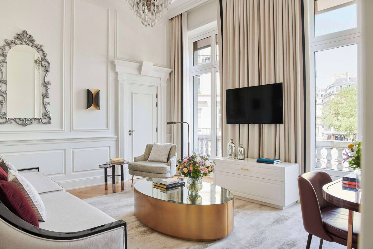 A modern living room with a sofa, a coffee table, a TV, and a large window with curtains.
