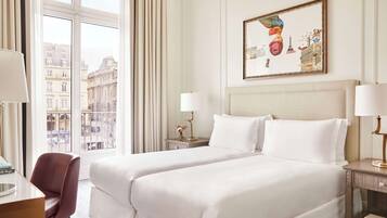 Habitación de hotel con una cama grande, dos mesitas de noche, un escritorio con una silla y una ventana con vista a la ciudad.