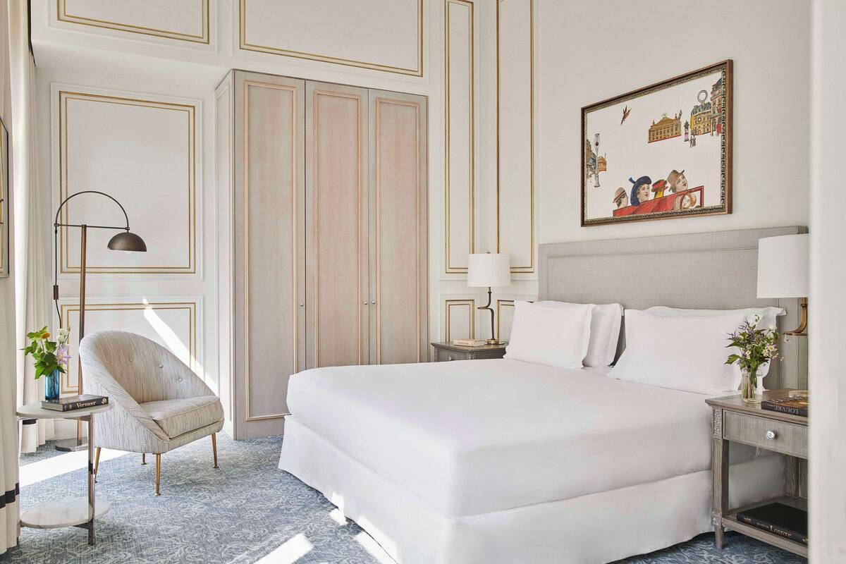 A hotel room with a large bed, a chair, a nightstand, and a wall with a framed picture.
