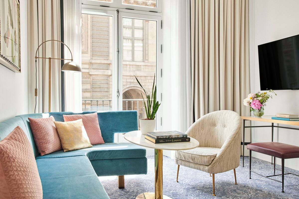 A modern living room with a blue sofa, a white armchair, a round coffee table, and a TV mounted on the wall.