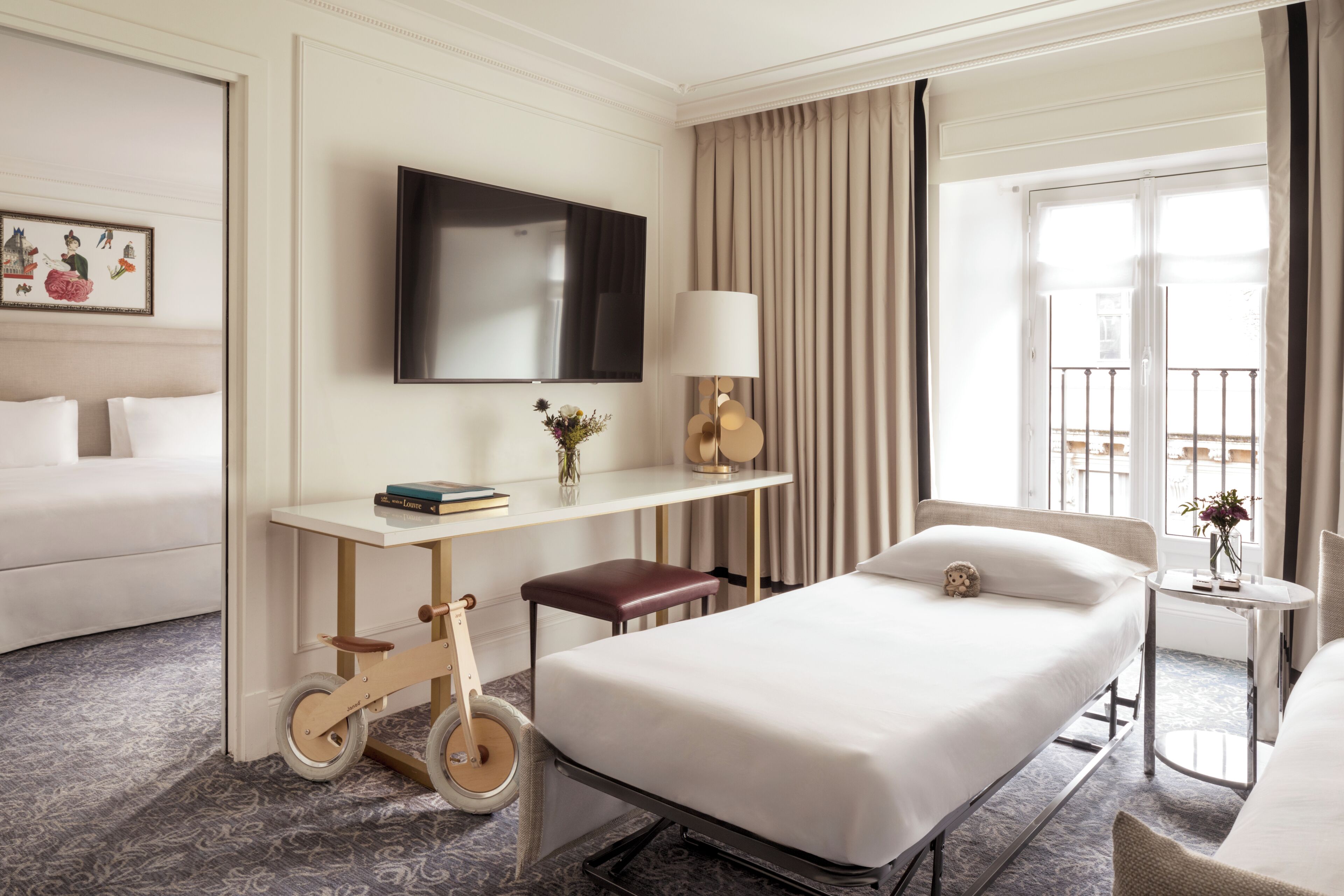 A hotel room with a bed, a desk with a chair, a television, and a window with curtains.