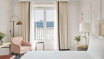Une chambre d’hôtel dotée d’un grand lit, d’un bureau avec une chaise, d’une table de chevet avec une lampe et offrant une vue sur la ville grâce à de grandes fenêtres.