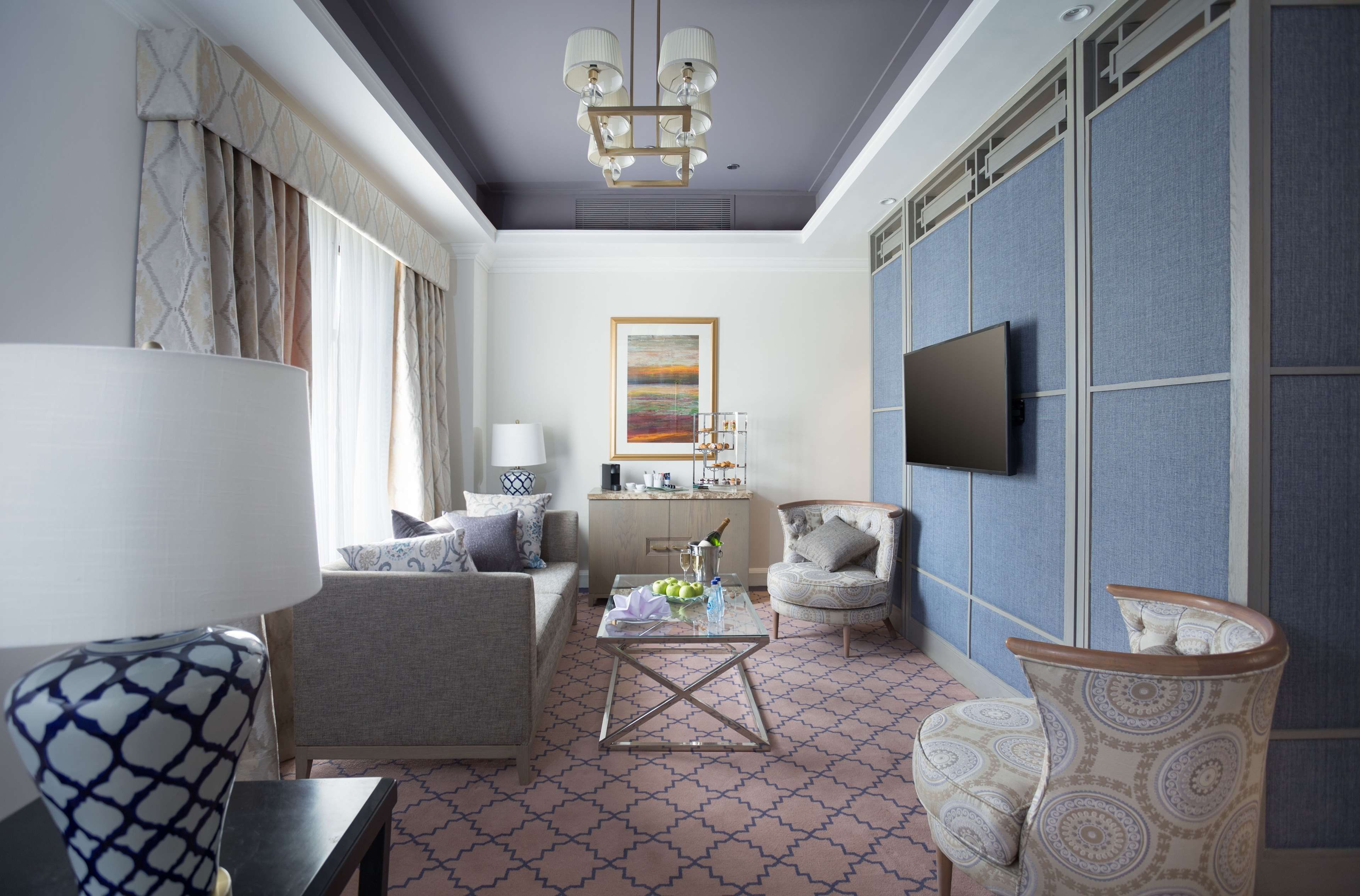 A modern living room with a sofa, armchairs, a coffee table, and a TV mounted on a blue partition wall.