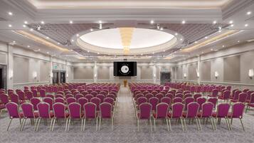 Un salón de conferencias con hileras de sillas moradas, una pantalla grande y un diseño de techo circular.