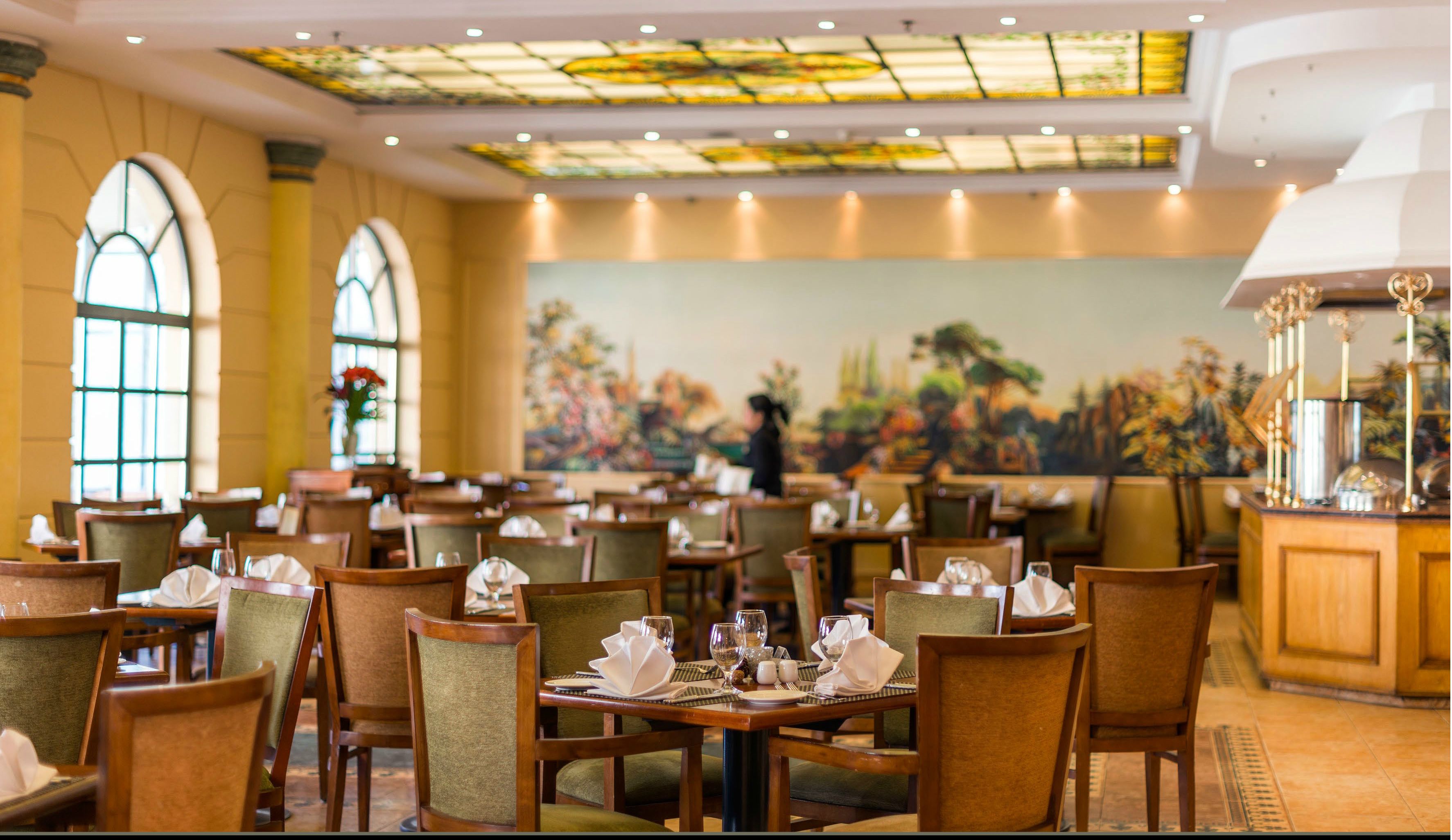 A restaurant with wooden tables and chairs, a mural on the wall, and a chandelier.