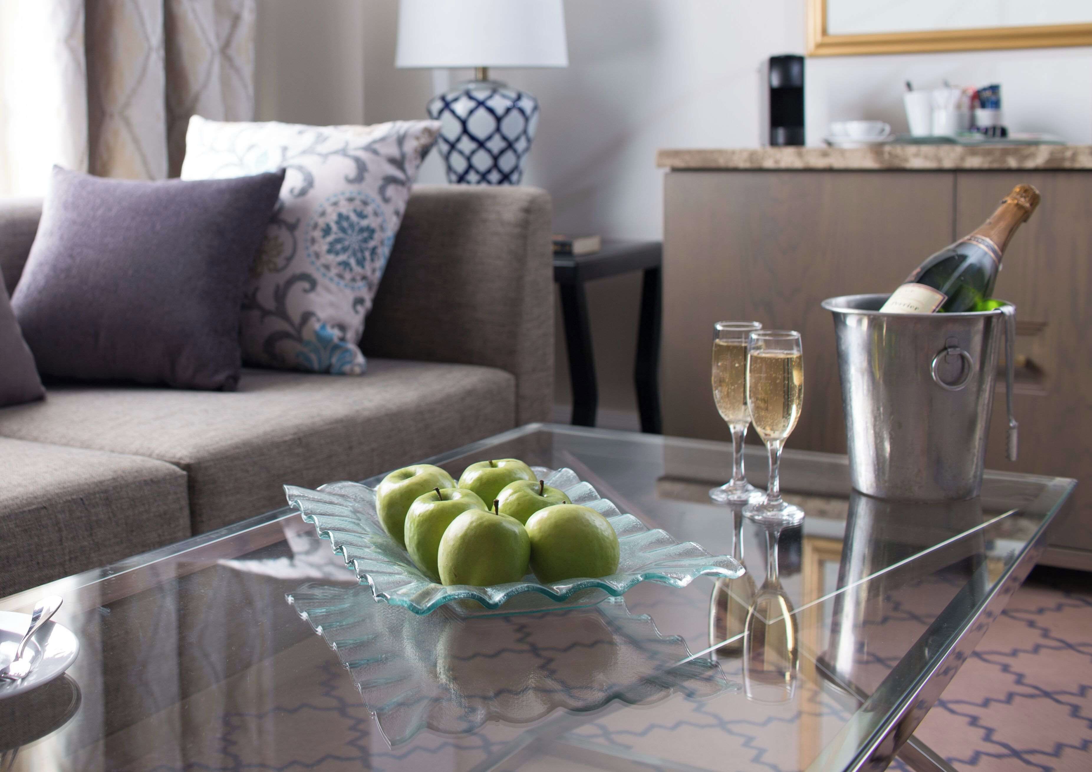 A glass table with a green apple tray, two champagne flutes, and a champagne bottle in a metal bucket.