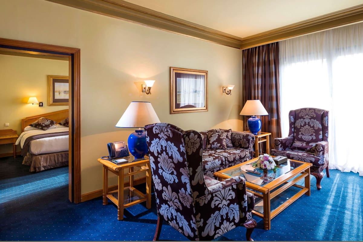 A hotel room with a bed, a sofa, two armchairs, a coffee table, and a desk with a phone.