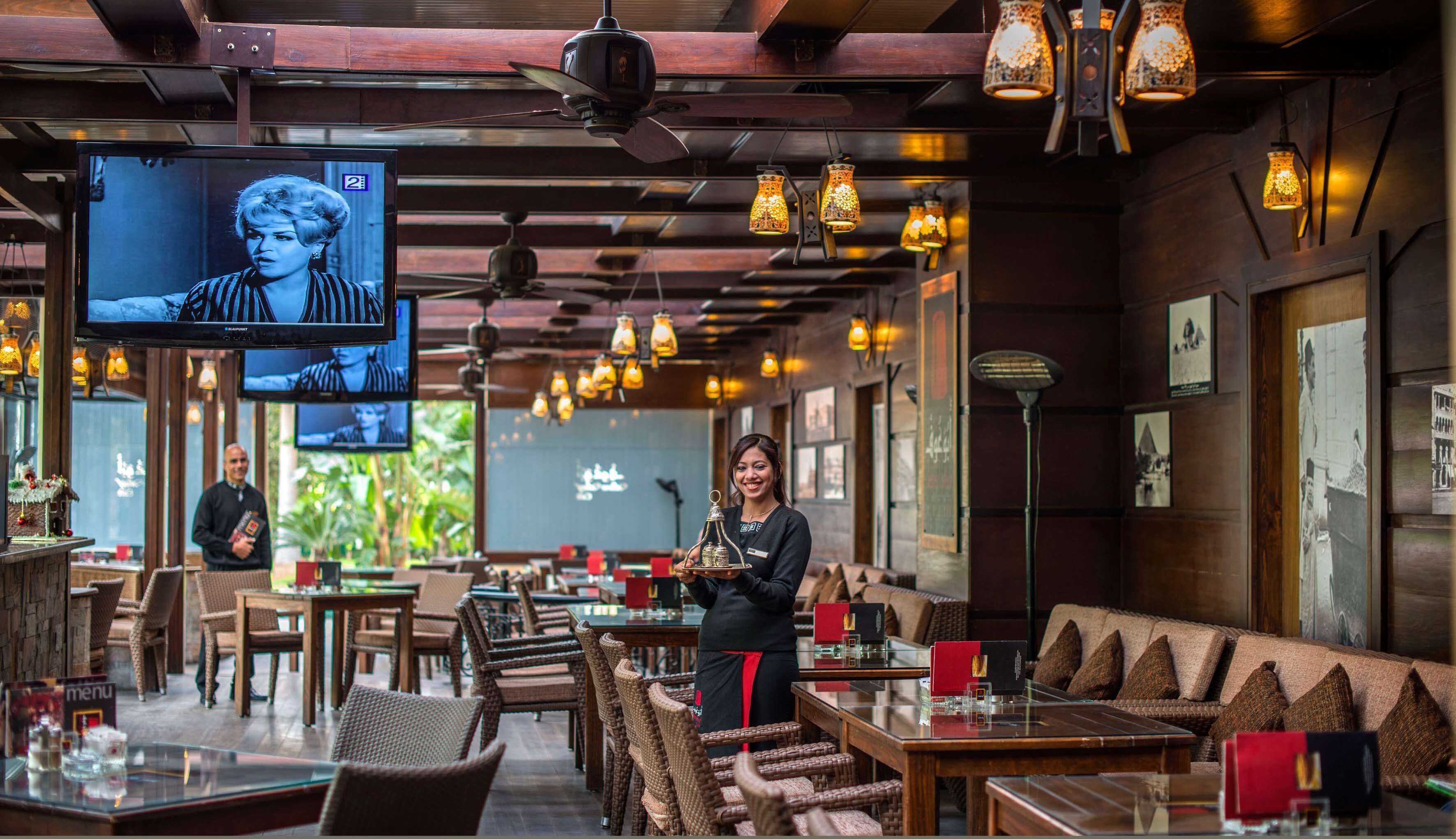 A restaurant interior with wooden furniture, hanging pendant lights, and a television displaying a program.