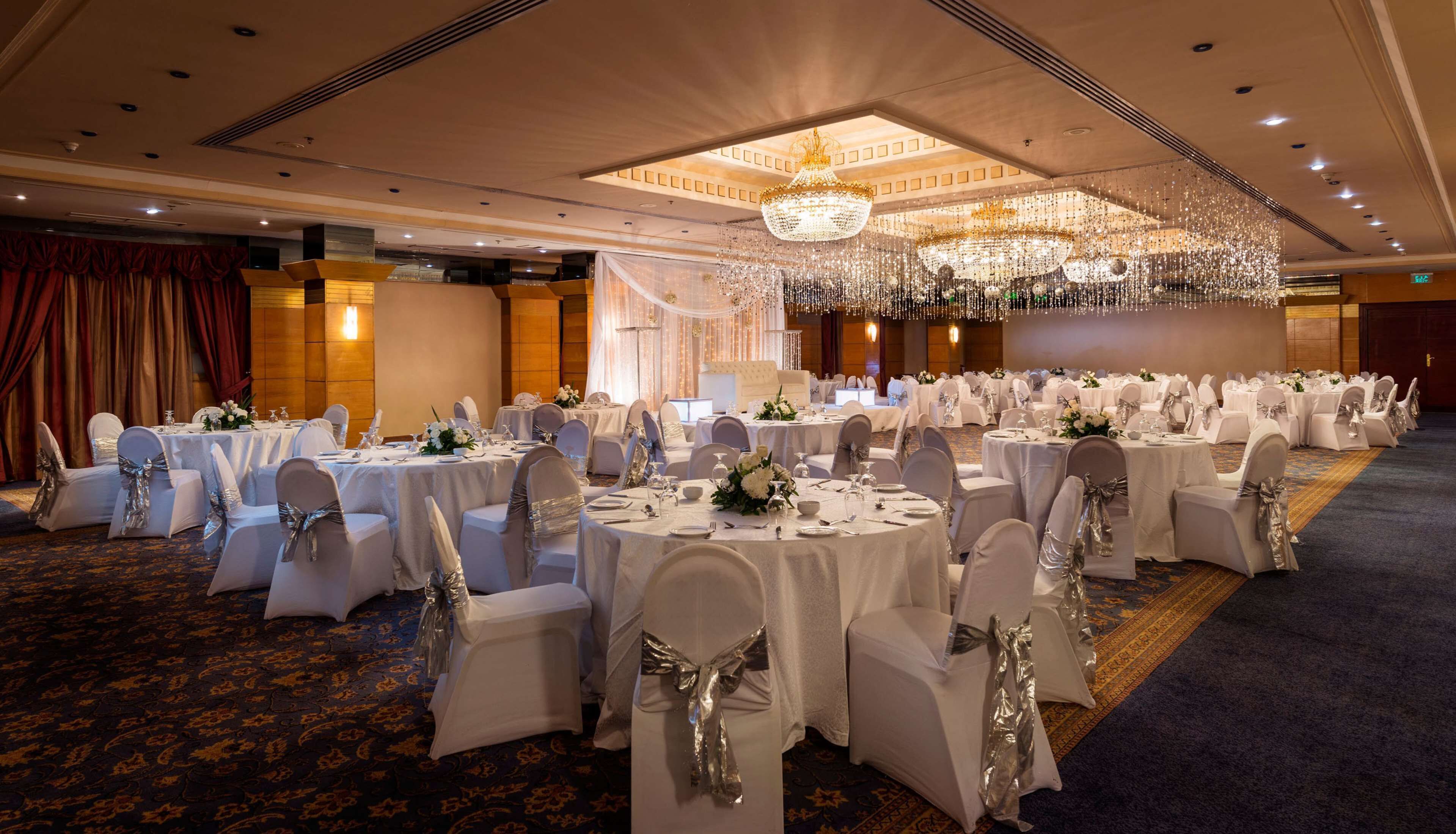 A banquet hall with round tables, white tablecloths, and silver chair covers.
