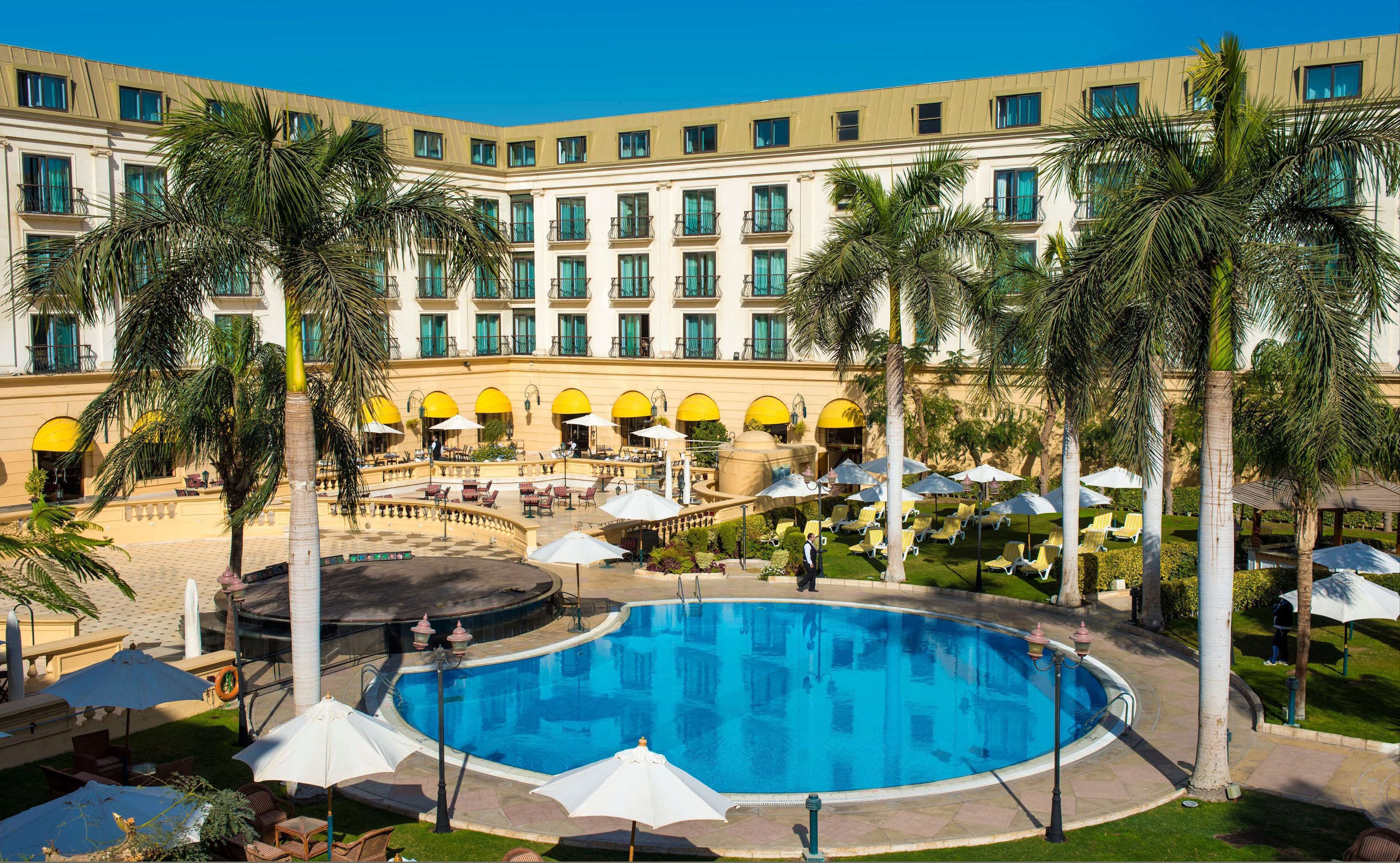 A hotel with a central pool, outdoor seating, and palm trees.