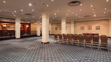 A large conference room with rows of chairs, a long table, and a staircase leading to another area.